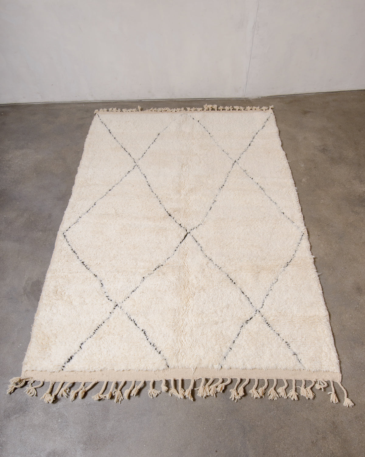 Cream Berber rug with black diamond design laying flat on floor.